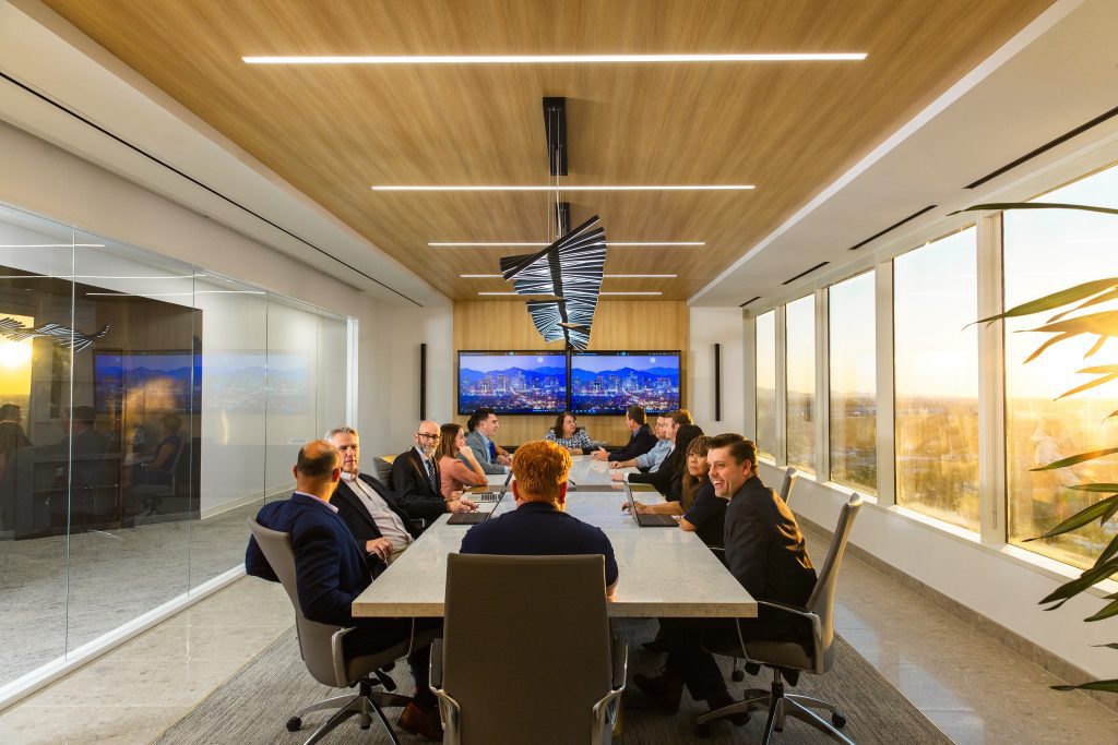 Perspective view of approximately 10 people conversing around a conference table.